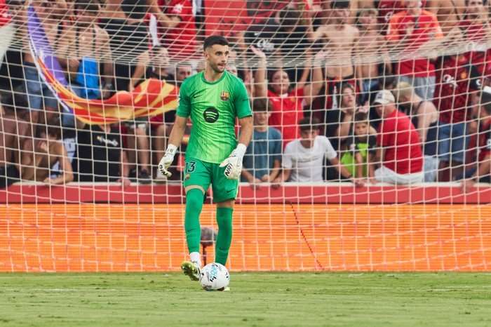 Joan Garcia, in green Barcelona goalkeeping kit and white gloves, looks for a pass as he controls a football with his feet.