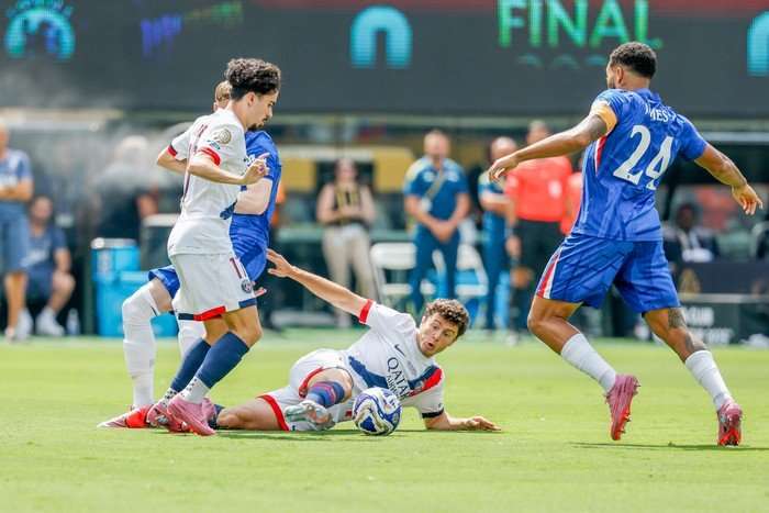 Jo&atilde;o Neves, in white, red and blue PSG football kit, makes a slide tackle with teammates and Chelsea players around him.