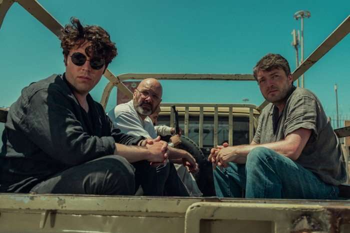 Tom Hughes as Declan Hughes, Johnny Harris as Eddie McKee and Tom Burke as Guy in Legends, sat in the back of an open-top truck in a sunny day.