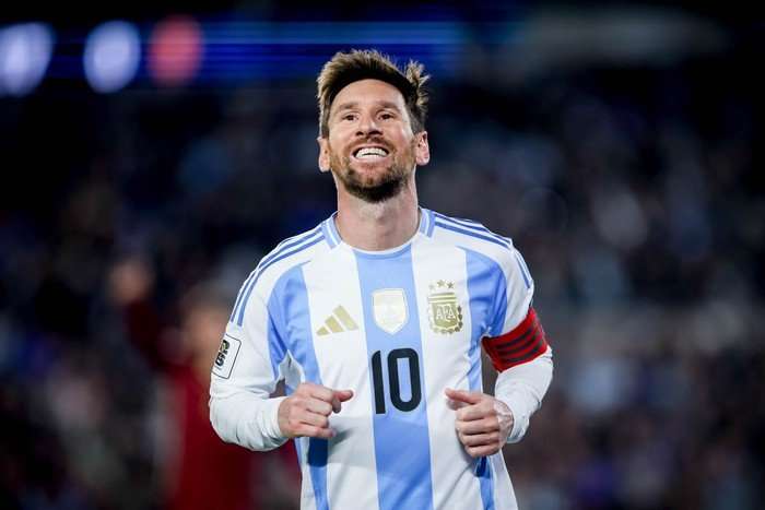 Lionel Messi Lionel Messi, in blue and white striped Argentina football kit, smiles wide as he jogs at Estadio Mas Monumental.