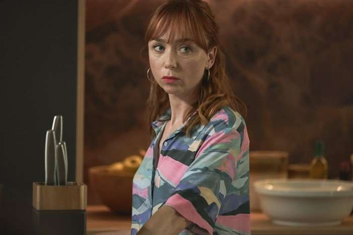 Little Disasters SE 1 EP 3 Emily Taaffe as Mel Quinn in Little Disasters looking angrily across the room, wearing a colourful patterned shirt.