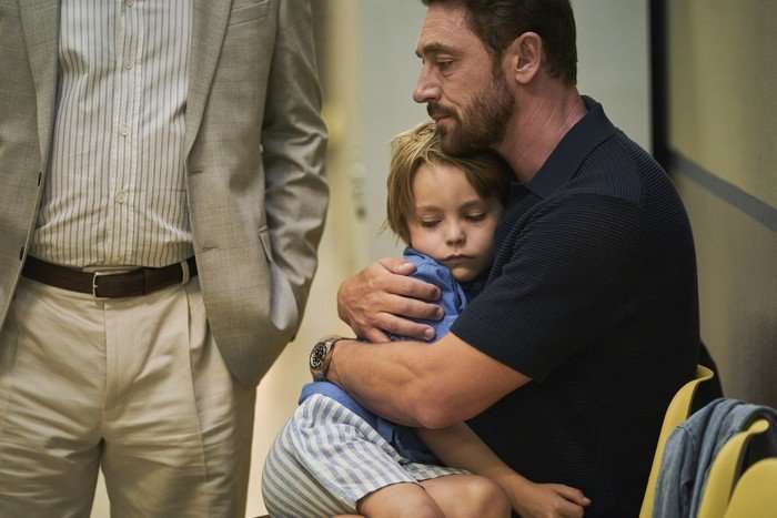 Little Disasters SE 1 EP 6 JJ Feild as Ed Carrisford holding Jax as Frankie in his arms, as they both look sad while sitting on a bench in a hallway.