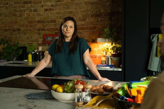 Little Disasters SE 1 EP 5 Jo Joyner as Dr Liz Burgess in Little Disasters leaning against a kitchen island, wearing a blue t-shirt.