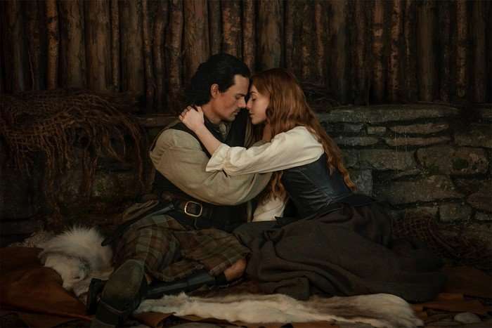 Outlander: Blood of My Blood - Season 2 202? Brian Fraser (Jamie Roy) and Ellen MacKenzie (Harriet Slater) in Outlander: Blood of My Blood season 2 embracing one another while sat down in a barn.