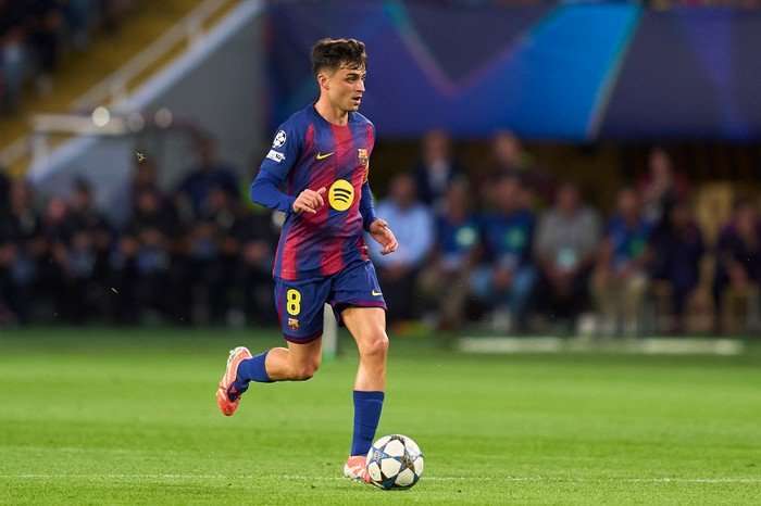 Pedri, in blue and red Barcelona kit, dribbles with the ball on the pitch at Estadi Olimpic Lluis Companys.