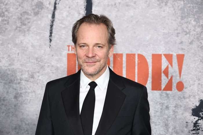 "The Bride!" New York Premiere Peter Sarsgaard on the red carpet, wearing a black suit and tie, smiling.