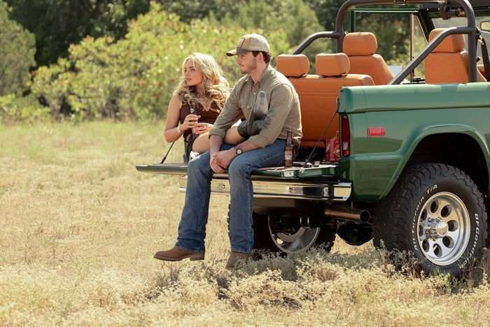 Natalie Alyn Lind as Oreana Lynn Jackson and Finn Little as Carter Green in Dutton Ranch, sat on the back of a pick-up truck. She is lounging with her legs on his lap.
