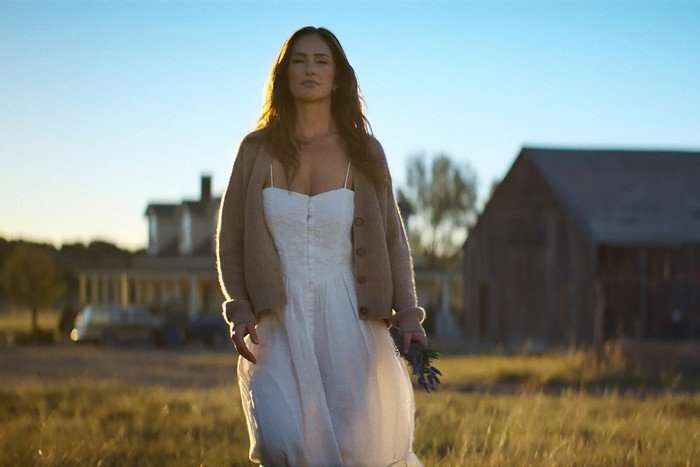 RANSOM CANYON SEASON 2 Minka Kelly as Quinn in Ransom Canyon walking across a field, wearing a white dress and cardigan.
