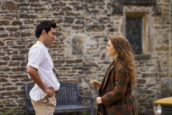 Rivals-Rupert-Taggie-Exclusive Alex Hassell as Rupert Campbell-Black and Bella Maclean as Taggie O'Hara in Rivals looking at each other by a car. The words "RT exclusive" are in the bottom right of the frame