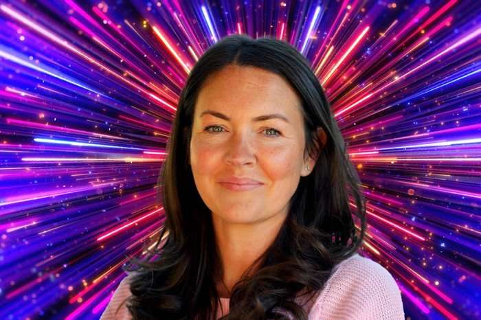 A picture of Lacey Turner smiling as she stands in front of a sparkly background.