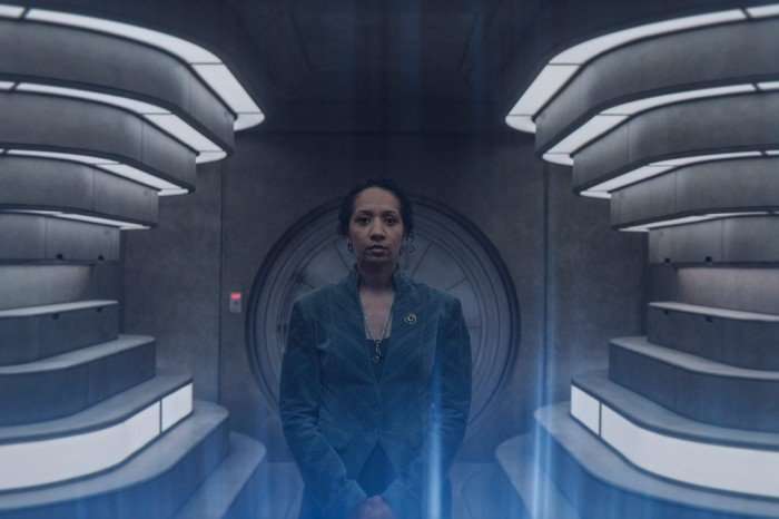 Alexandria Riley as Camille Sims in Silo season 3. She's standing in a futuristic tunnel.