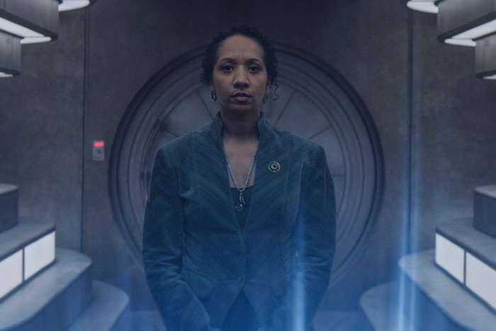 Alexandria Riley as Camille Sims in Silo season 3. She's standing in a futuristic tunnel.