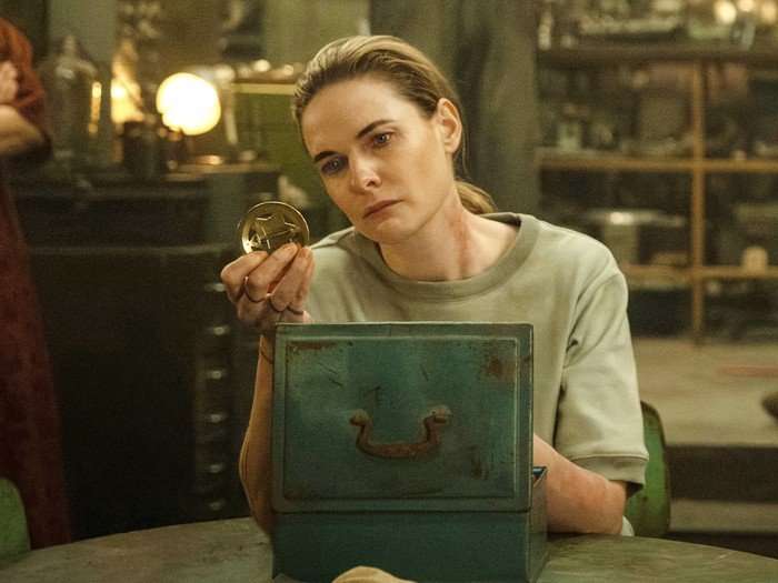 Rebecca Ferguson as Juliette in Silo season 3. She's sat down with an open box in front of her, examining something thoughtfully.