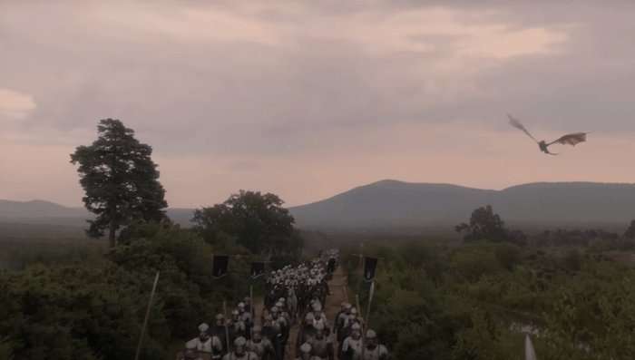 House of the Dragon Tessarion A wide shot of an army marching with Hightower banners through a rural setting as a blue dragon Tessarion flies overhead in House of the Dragon season 2.