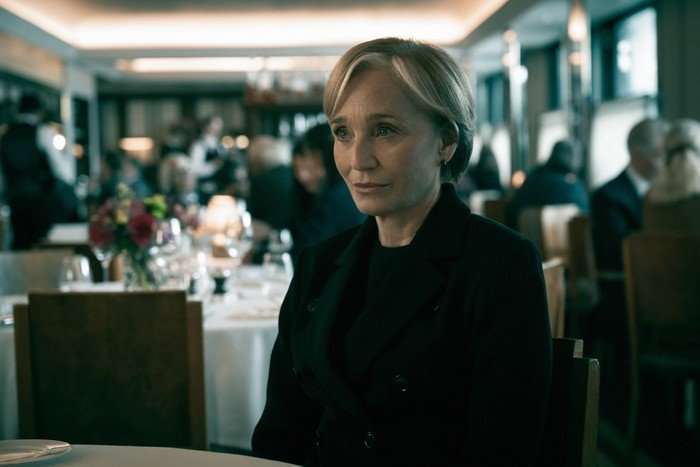 Slow Horses Kristin Scott Thomas in Slow Horses, wearing all black and sat at a table in a restaurant.