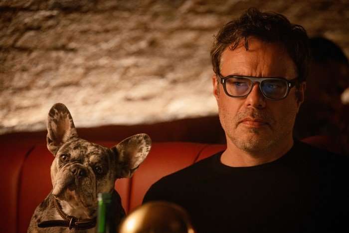Steve sits in a booth in a dimly lit bar, with his cute little French Bulldog next to him