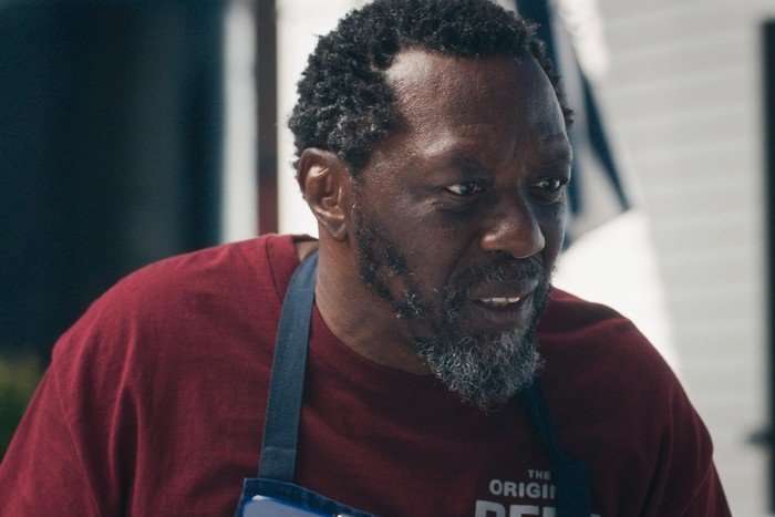 Still 2025-05-21 162055_1.1.12R Edwin Lee Gibson as Ebraheim in The Bear, wearing a red t-shirt and a blue apron.