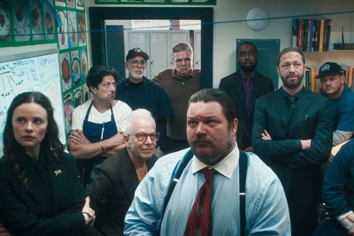 The cast of The Bear, stood in an office room together, all looking forward at a wall.