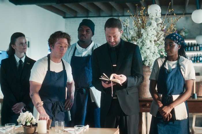TBR4_412_SMLS_250513.mov.01_27_39_21.Still034_R Sarah Ramos, Jeremy Allen White, Lionel Boyce, Ebon Moss-Bachrach and Ayo Edebiri in The Bear, stood together in the restaurant. Richie is looking at a small book and the others are looking at him.