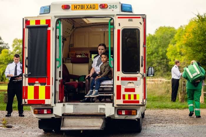 Jahsaiah Williams as Alex Hanscombe in The Witness sat in the back of an ambulance, being comforted by a police officer who sits behind him and is wearing a blood-stained shirt.