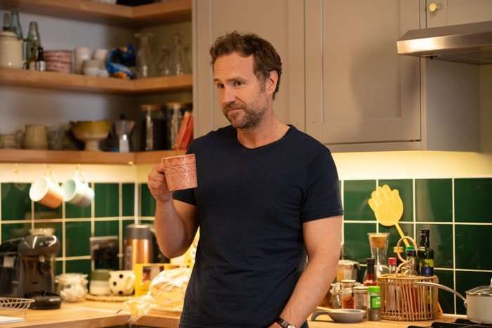 Rafe Spall in Trying in a kitchen holding a mug