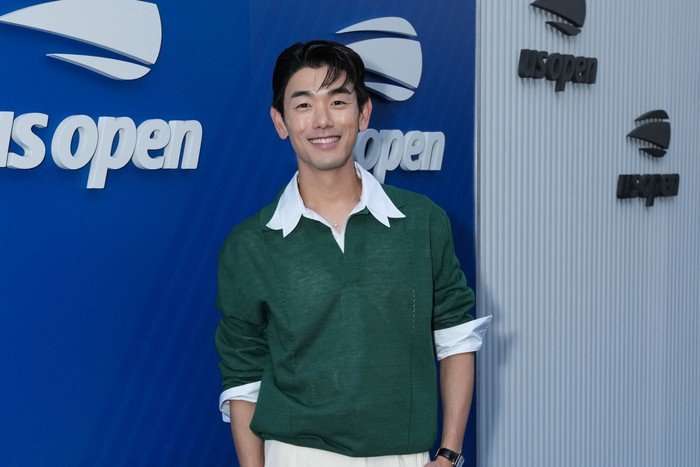 the-traitors-US-eric-nam Eric Nam wearing a green jumper, stood and smiling ahead with one hand in his pocket.