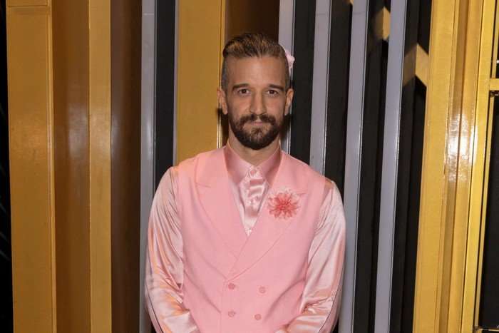 the-traitors-US Mark Ballas wearing a matching pink suit and shirt, stood with his hands clasped in front of him and smiling ahead.