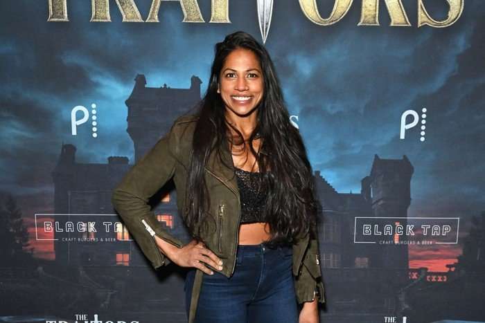 the-traitors-US Natalie Anderson smiles ahead with one hand on her hip.