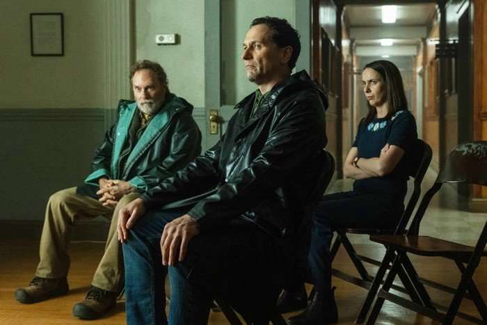 Stephen Root, Matthew Rhys and Kate O&rsquo;Flynn in Widow&rsquo;s Bay, sat on chairs together. Root and Rhys are wearing wet raincoats.