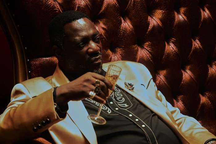 Adewale Akinnuoye-Agbaje sat as Alamo Brown in a dark interior holding a drink in the Euphoria season 3 finale.