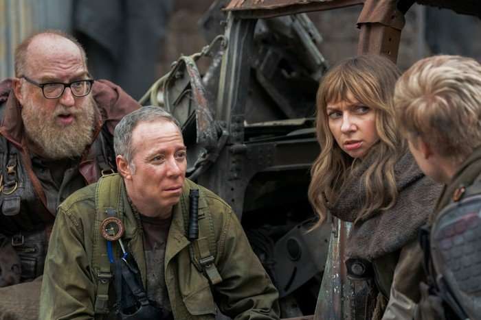 Bert, Stuart and Denise wear dark green military-style garb in a drab location, as they look irritated at someone in their group