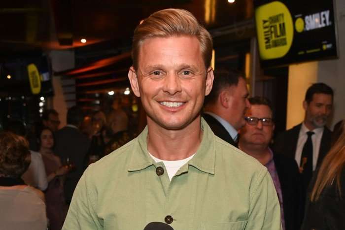 A blonde man wearing a green shirt, smiling ahead.