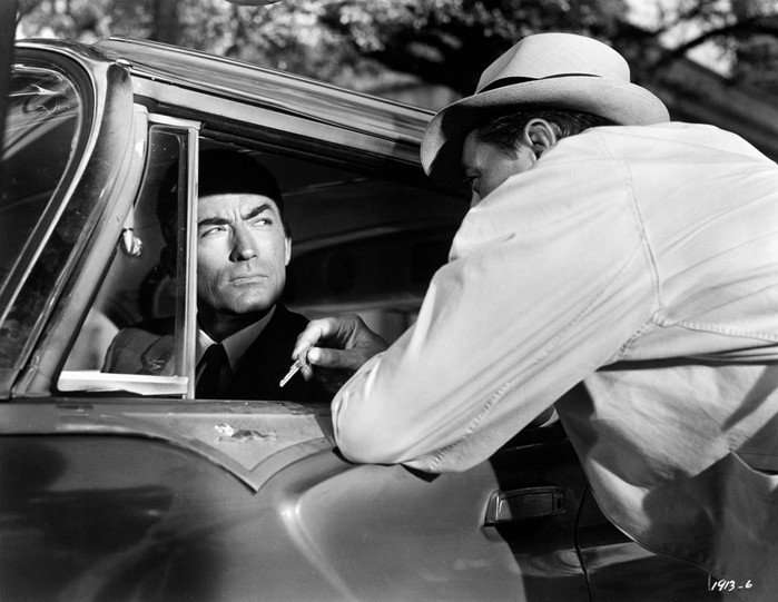 Gregory Peck and Robert Mitchum in Cape Fear Gregory Peck’s Sam Bowden, wearing a dark suit and tie, stares suspiciously from the driver’s seat of a car as Robert Mitchum’s Max Cady, in a light jacket and brimmed hat, leans into the open window holding out a set of keys in Cape Fear (1962).