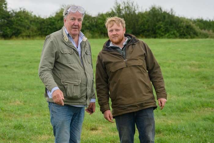 clarksons-farm (3) Jeremy Clarkson and Kaleb Cooper stood next to each other in a grassy woodland, wearing green jackets and blue jeans.