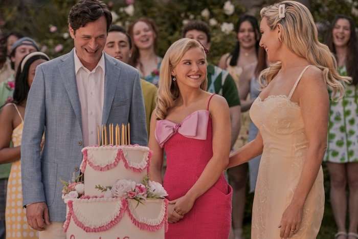 Tom Everett Scott, Lexi Minetree, June Diane Raphael in Elle standing by a big pink birthday cake, smiling as Lexi prepares to blow out the candles.