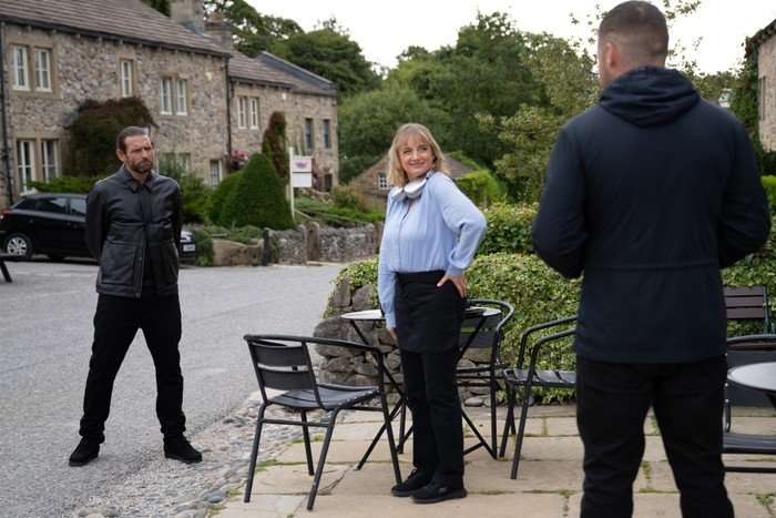 Nicola looking at Aaron as Kev stands across from him with arms folded in Emmerdale
