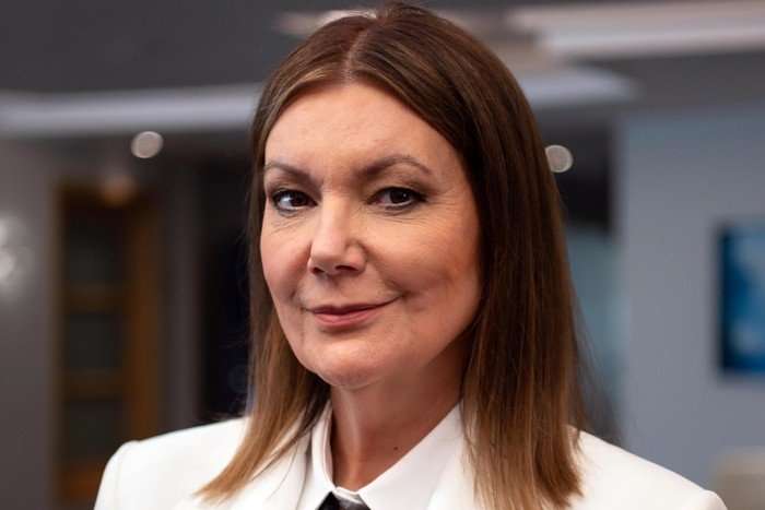 THE GOOD SHIP MURDER: - Series 4 Fiona Allen as Captain Serena Teller in The Good Ship Murder season 4. Wearing a white blazer and matching shirt, she looks directly at the camera with a composed, authoritative expression. The softly blurred ship interior behind her reflects the character's polished and commanding presence.