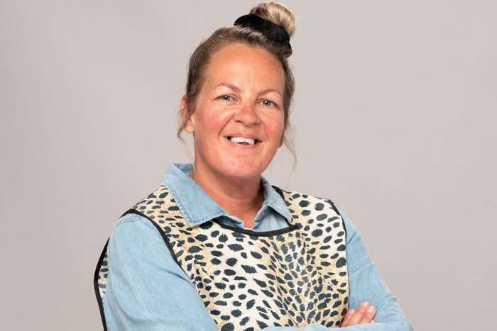 lorraine-stanley Lorraine Stanley as Karen Taylor. She is wearing a blue shirt and leopard print overall. She is smiling.