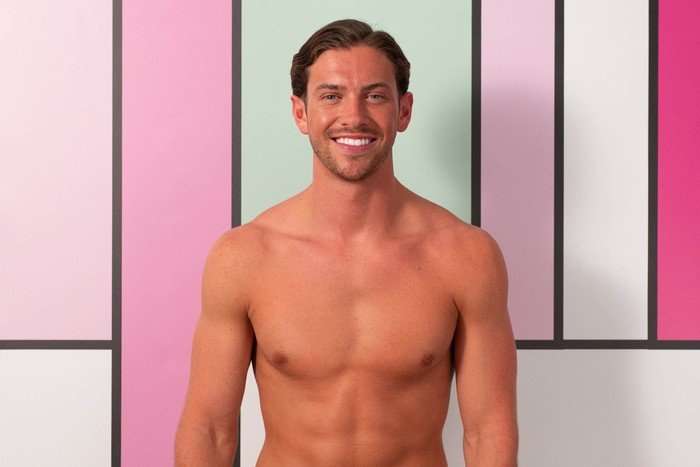love-island (40) A topless man posing in front of a pastel pink and green colour block background.