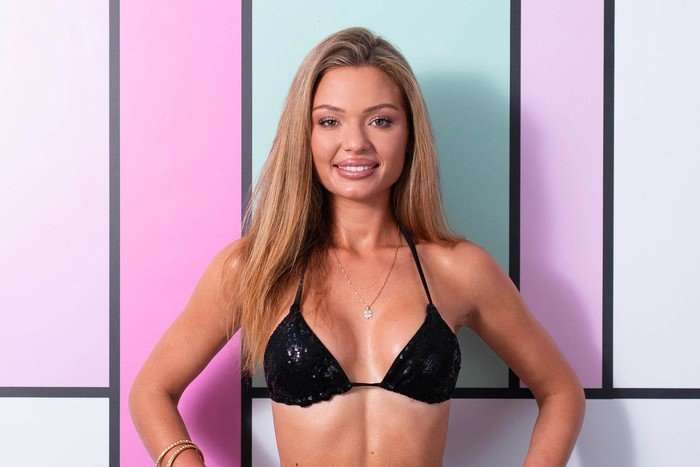 Julia stands smiling and wears a black bikini. She has blonde hair.