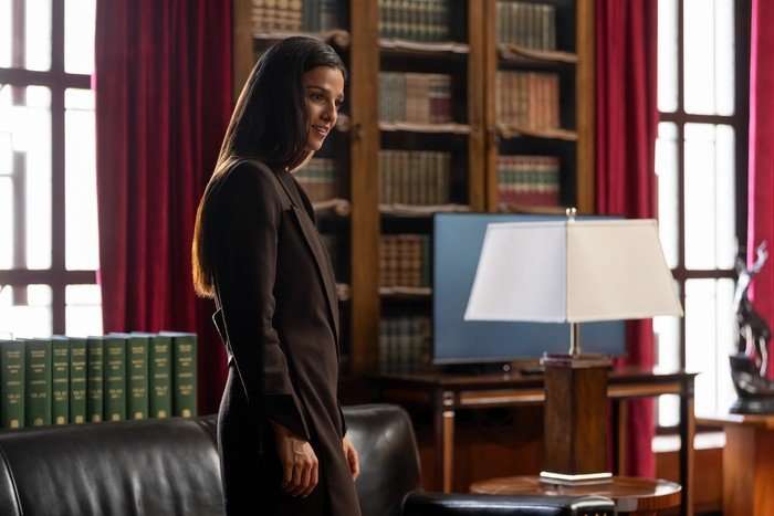 Industrymarisa-abela_4 (1) Marisa Abela in Industry season 4, standing up in a book-lined office, wearing a brown blazer and looking expectantly at someone.
