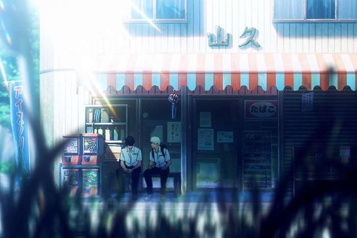 The Summer Hikaru Died A sunlit anime scene shows two teenage boys in white school uniforms sitting on a bench outside a small neighborhood shop. One boy has dark hair and looks down at his hands, while the other, with light-colored hair, turns toward him as if speaking. The storefront has a red-and-white striped awning, vending-style machines, and Japanese signs, including a tobacco sign near the entrance. Bright lens flares and soft summer lighting wash over the scene, while blurred grass in the foreground creates a quiet, nostalgic atmosphere.