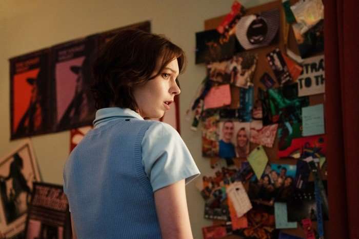 Pip stands in her bedroom, turning toward a cluttered noticeboard covered in photos, notes and keepsakes. Warm, low lighting creates a tense atmosphere as she looks shocked or alarmed, suggesting she has just discovered something unsettling. The room is filled with personal touches, while the blurred posters and pinned memories in the background hint at her investigative nature and emotional connections.