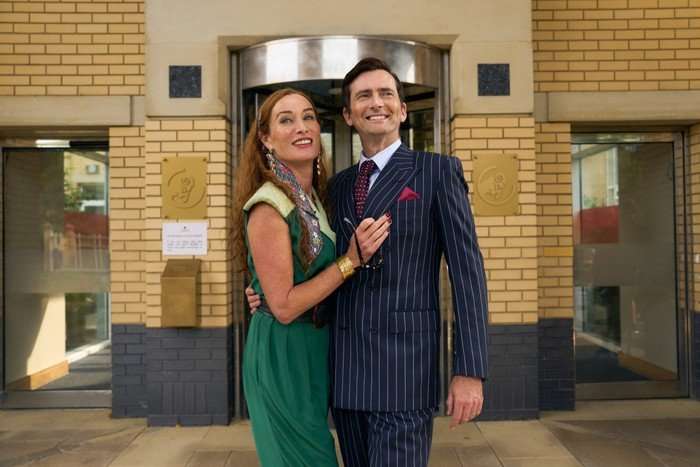 RIVALS 2 Victoria Smurfit and David Tennant standing in front of the Corinium offices, smiling for cameras and embracing.