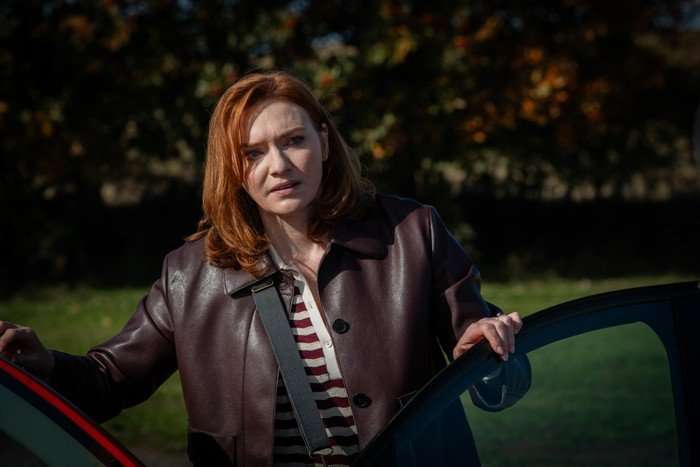 Eleanor Tomlinson as Amanda Blakefield in The Fortune standing besides her car with the door open, looking out at something and seeming confused.