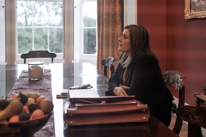 The Fortune Nina Wadia as Laura Mistry in The Fortune sitting at a dining table with a briefcase and folders in front of her, talking.