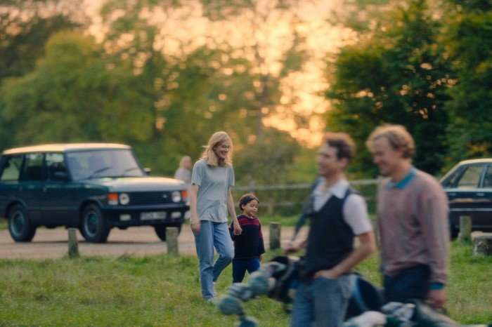 Eleanor Williams as Rachell Nickell and Jahsaiah Williams as Alex Hanscombe in The Witness, walking through a park on a sunlit day.