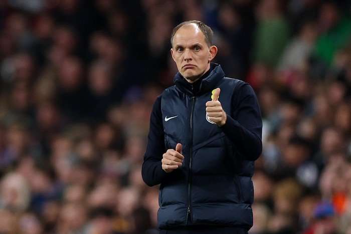 England head coach Thomas Tuchel standing on the sidelines with a thumbs-up. In the background, there are crowds out of focus.