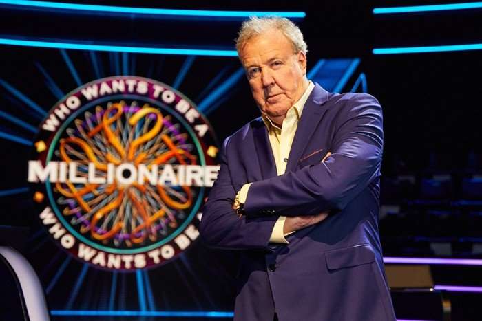 Jeremy Clarkson on Who Wants to Be a Millionaire? Jeremy Clarkson stood wearing a blue suit with his arms folded looking ahead.