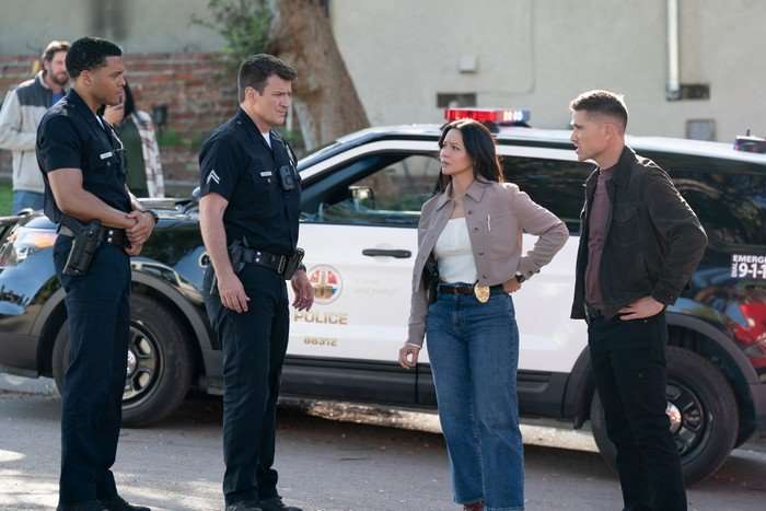 The Rookie Deric Augustine as Miles Penn, Nathan Fillion as John Nolan, Melissa O’Neil as Lucy Chen and Eric Winter as Tim Bradford in The Rookie, stood outside by a police car.